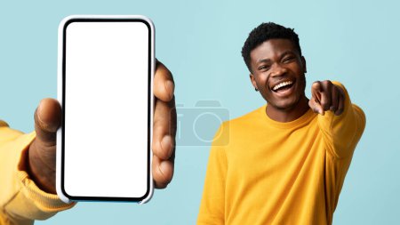 Photo for Smiling millennial african american guy pointing finger at camera, near hand with phone with empty screen, isolated on blue background, studio, collage. Fun, humor app, website - Royalty Free Image