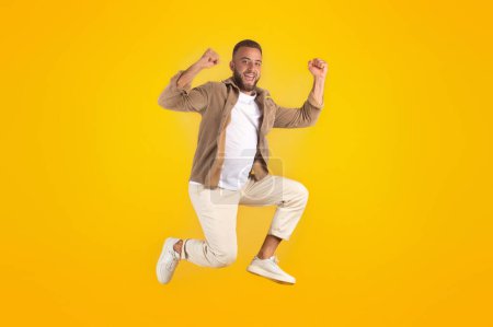 Photo for Glad millennial caucasian man with beard in casual has fun, jumping, freezes in air, celebrate win, isolated on yellow studio background. Victory, lifestyle and human emotions, ad and offer - Royalty Free Image