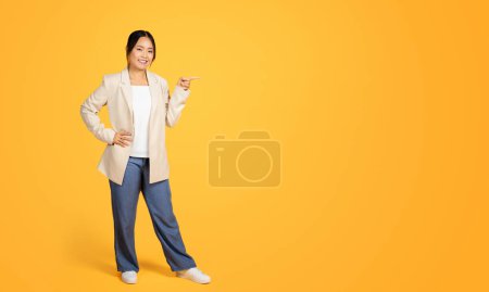 Foto de Señora milenaria china positiva, apunte con los dedos al espacio de copia, aislado sobre fondo de estudio naranja, longitud completa. Expresión, mensaje o idea, venta, anuncio y oferta para negocios, trabajo - Imagen libre de derechos