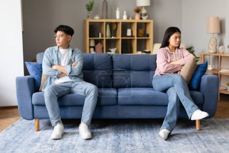 Photo for Korean couple sitting upset and offended, distancing themselves after argument in the living room, looking at sides and thinking about divorce. Relational challenges and unresolved conflicts - Royalty Free Image