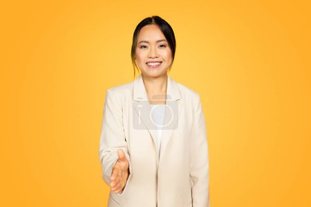 Photo for Smiling friendly millennial Asian woman, isolated on yellow, extends her hand invitingly for handshake. Her welcoming, open posture and genuine smile speak of friendliness and positive connections - Royalty Free Image