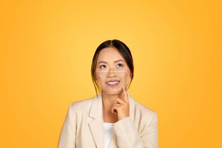 Photo for Immersed in her thoughts, an Asian woman exhibits contemplative expression, eyes gently lifted upwards in reflection, isolated on yellow background, studio. Encapsulating in thought - Royalty Free Image