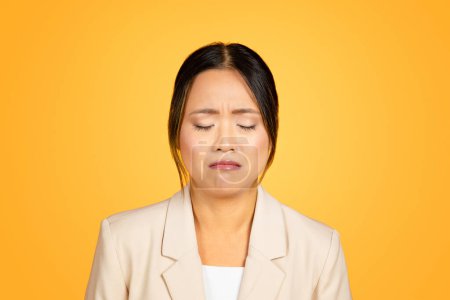 Photo for Upset emotional young Asian woman, with tears streaking down her cheeks, shows a vulnerable moment of sadness, dramatically juxtaposed against orange studio background, close up - Royalty Free Image