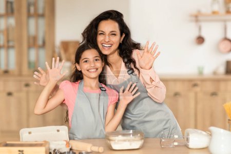 Foto de La mamá positiva y el niño de la hija alegremente mostrando sus manos en harina después de amasar la masa en la cocina moderna. Padres alegres y niños haciendo galletas, disfrutando de la diversión horneando juntos - Imagen libre de derechos