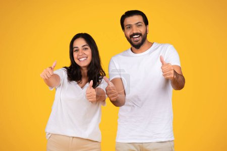 Téléchargez les photos : Un jeune couple arabe enthousiaste montre les pouces levés, isolé sur fond de studio jaune. Expressions et gestes montrent l'approbation et la positivité, ce qui rend l'atmosphère amusante et édifiante - en image libre de droit