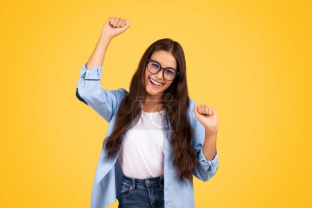 Photo for Glad shocked european teen woman in glasses exuberant celebrates win, rise fists, isolated on yellow background studio. Bright victorious emotion, woman enjoy success, great news - Royalty Free Image