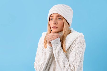 Photo for Young woman suffering from cold, freezing lady wearing knitted sweater and hat, holding hands next to mouth, standing over blue studio background - Royalty Free Image