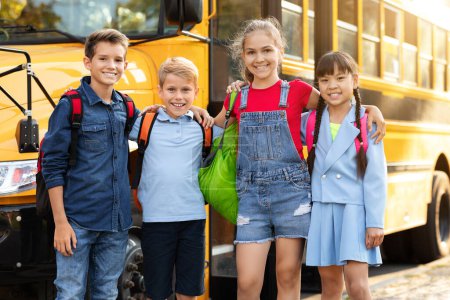 Foto de Grupo de niños felices de pie junto al autobús escolar amarillo, retrato de pequeños amigos alegres con mochilas abrazando y sonriendo a la cámara, anticipando una aventura en el aprendizaje y la amistad - Imagen libre de derechos