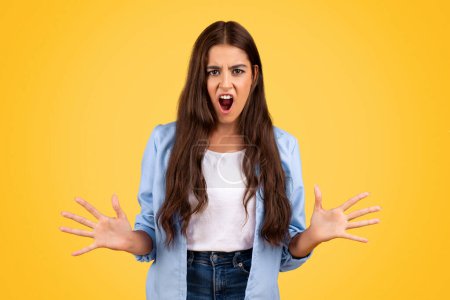 Photo for Angry upset teen embodies youthful angst against stark with open mouth, isolated on yellow background. Expressive face and tensed posture reflect of adolescent emotions, gesture - Royalty Free Image