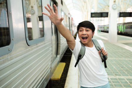Foto de Estresado joven viajero asiático hombre estudiante con mochila corriendo por la plataforma de la estación de tren, chico taiwanés persiguiendo tren de salida. Turista tarde en viaje en avión - Imagen libre de derechos