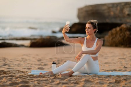 Photo for Amidst the calming sound of waves, a woman engrossed in her yoga routine takes a moment to snap a photo, with the sun setting near a cliff, free space - Royalty Free Image
