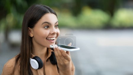 Photo for Excited beautiful young woman student with wireless headphones record voice message for her friend or lover on smartphone, looking at copy space, have break at university campus, panorama - Royalty Free Image