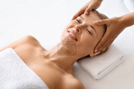 Photo for Beautician making gentle acupressure head massage to graceful middle aged woman peacefully lying on table at spa salon, beautiful mature female enjoying relaxation and wellness, above view - Royalty Free Image