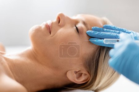 Photo for Relaxed middle aged woman at spa salon, receiving a careful injection to the eye wrinkle zone, professional beautician fixing age-related skin concerns for attractive mature lady, closeup shot - Royalty Free Image