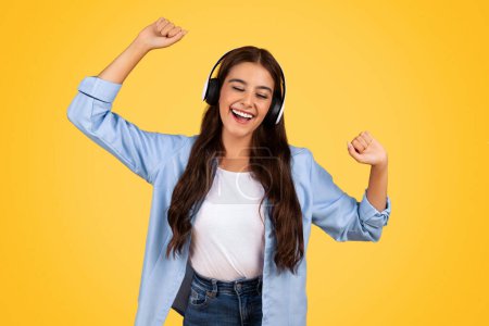 Photo for Cheerful teen student with closed eyes immerses in favorite tunes, embodying carefree, upbeat student lifestyle with headphones, sing song, isolated on yellow background. Rest, relax at spare time - Royalty Free Image