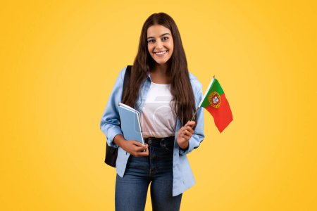 Photo for Smiling caucasian teen student woman, with Portugal flag, combines patriotism with academia, isolated on yellow background. Lifestyle, national pride and exchange study, learning Spanish - Royalty Free Image