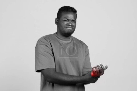 Photo for Young african guy suffering from wrist pain touching and pressing hand to red pain spot in studio, black and white shot. Sport injuries and traumas, chronic arthritis and carpal tunnel syndrome - Royalty Free Image