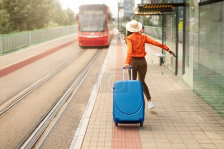 Téléchargez les photos : Raté le tramway. Jeune femme avec valise pressée, courant pour attraper le tram à un arrêt de ville animé, étant en retard. Les trajets quotidiens urbains et la lutte contre le temps. Espace de copie - en image libre de droit