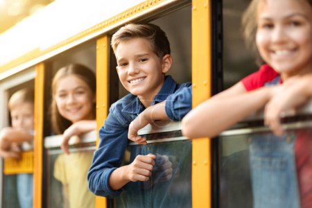 Foto de Niños emocionados espiando desde la ventana del autobús escolar, grupo de niños felices mirando y sonriendo a la cámara, compañeros de clase positivos listos para embarcarse en su viaje, enfoque selectivo en el niño - Imagen libre de derechos