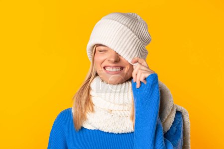 Photo for Joyful young woman in knitted hat, closing one eye, exuding radiant smile in sunlit yellow studio, emanating playful, carefree spirit, representing lighthearted, spirited youthfulness and fun - Royalty Free Image
