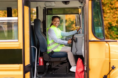 Foto de Conductora negra alegre sentada en el autobús escolar amarillo, señora afroamericana feliz en uniforme amistoso sonriendo hacia la cámara a través de la puerta abierta del vehículo, expresando positividad y seguridad, espacio libre - Imagen libre de derechos