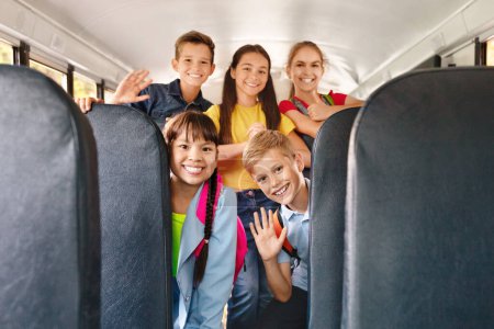 Photo for Diverse happy cheerful kids having fun inside a school bus, waving enthusiastically at the camera, smiling pupils posing together, sharing joyful moments during their ride to school - Royalty Free Image
