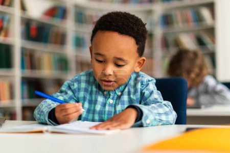 Téléchargez les photos : Un écolier noir écrit dans son copybook lors d'une leçon instructive en classe primaire dynamique, illustrant un moment d'engagement actif et d'attention au développement éducatif - en image libre de droit