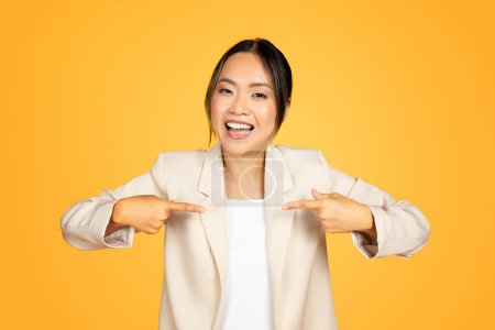 Photo for Self-assured Asian woman, with fingers confidently pointing towards herself, showcases a bold and empowering demeanor. Her expressive eyes and steady stance tell story of self-belief and assurance - Royalty Free Image