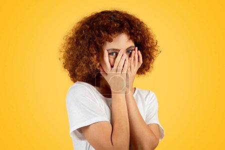 Photo for Positive teen caucasian woman, flushed with embarrassment, covers face with hands, isolated on yellow background, studio, close up. Moment of youthful bashfulness, lifestyle - Royalty Free Image