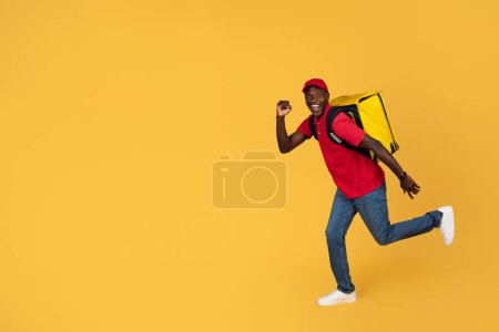 Photo for Glad funny young black delivery man in uniform and cap with big backpack run, has fun, isolated on orange studio background, full length. Recommendation express delivery service, fast order - Royalty Free Image