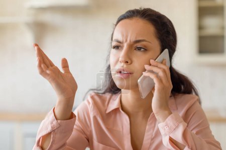 Photo for Upset woman in pink blouse conversing on her mobile phone, gestures with her hand, displaying a sense of disagreement or misunderstanding during the call - Royalty Free Image