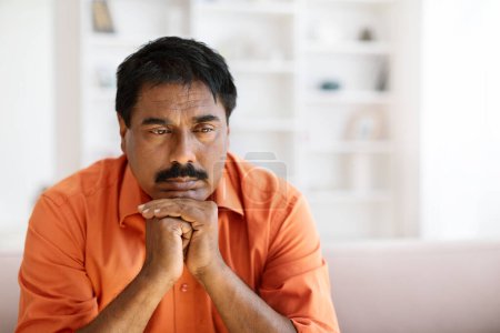 Photo for Closeup of depressed unhappy upset indian middle aged man with moustache sitting on couch at home. Hindu man feeling lonely, experiencing breakup or divorce. Anxiety, mental disorder, copy space - Royalty Free Image