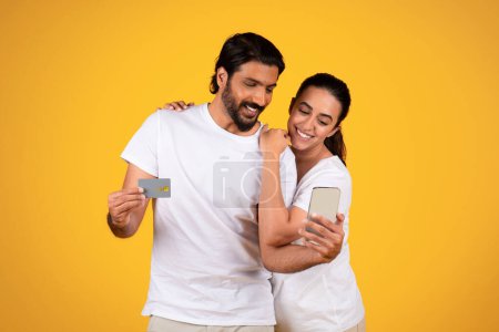 Photo for Smiling middle aged mature couple hold credit card and smartphone, isolated on yellow studio background. Online shopping, sale app, banking finance, money for shopaholic, pay order - Royalty Free Image