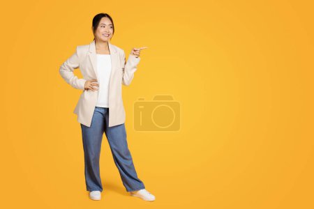 Photo for Positive korean millennial woman, point finger at empty space, isolated on orange studio background, full length. Idea, sale attention, ad and offer for business, work and study - Royalty Free Image