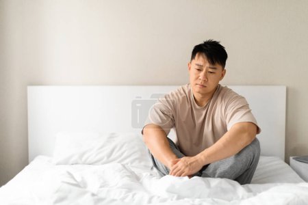Photo for Frustrated mature chinese man in pajamas sitting on bed at home, thinking about something, looking for solution while crisis, suffering from divorce, breakup, panorama with copy space - Royalty Free Image