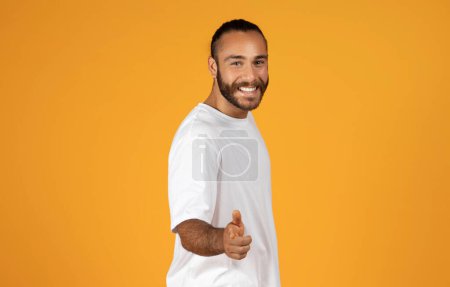 Foto de Sonriente hombre europeo seguro de sí mismo, confianza, señala con el dedo a la cámara, captar la atención del espectador y hacer declaración audaz, motivado a la decisión, aislado en fondo de estudio naranja - Imagen libre de derechos