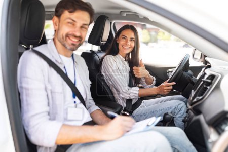 Photo for Handsome millennial man instructor examinating brunette lady student at driving school, taking notes at chart while sitting by smiling young woman driving auto and waiting for test results, copy space - Royalty Free Image