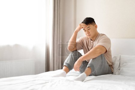 Photo for Despaired sad lonely middle aged asian man sits on white bed and thinks in bedroom interior, empty space. Stress, problem, depression and bad news at home, midlife crisis - Royalty Free Image