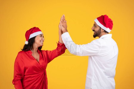 Photo for Happy mature latin family in Christmas hat, give high five with hands, isolated on yellow background, studio. Win, holiday season, love and celebration New Year together, success - Royalty Free Image