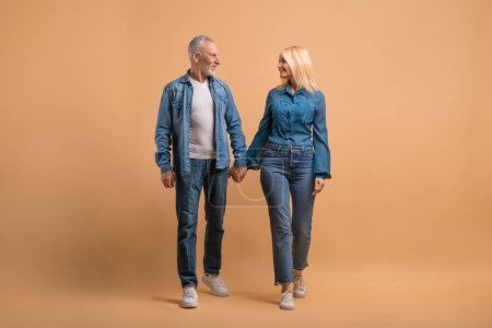 Photo for Loving happy senior couple holding hands and walking together isolated on beige studio background, looking at each other, have conversation. Elderly man and woman have romantic date, full length - Royalty Free Image