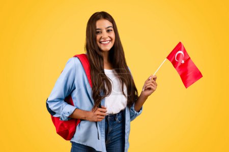 Photo for Smiling european young student woman, with Turkish flag, combines patriotism with education, isolated on yellow background. Lifestyle, national pride and exchange study, learning Turkey - Royalty Free Image