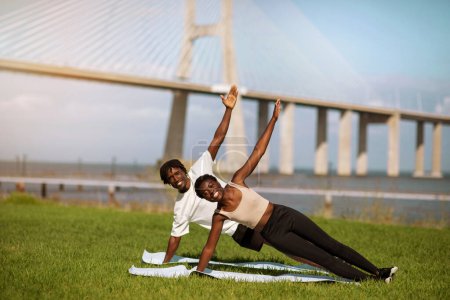 Photo for Sporty black man and woman training yoga in side plank pose outdoors, young african american couple in sportswear exercising together on mats, enjoying outside workouts, copy space - Royalty Free Image