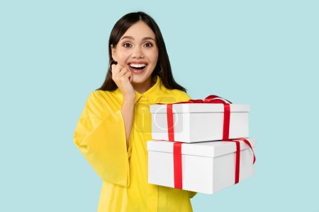 Photo for Emotional gorgeous young brunette model holding gift boxes over blue studio background, free space. Pretty millennial lady with Womans Day or birthday presents. Shopping for spring holiday concept - Royalty Free Image
