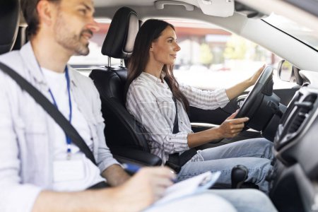 Photo for Cheerful confident pretty young lady sitting inside car with man instructor by her side, woman student holding hands on steering wheel, passing exams successfully at driving school, getting license - Royalty Free Image