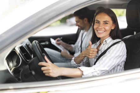 Photo for Happy pretty young woman sitting inside car with man instructor by her side, lady student at driver seat showing thumb up, passing exams successfully at driving school, getting license - Royalty Free Image