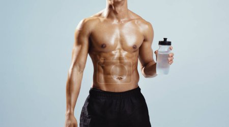Photo for Hydration. Unrecognizable Fitness Guy With Shirtless Torso And Perfect Abs Holding Bottle Of Water Drink During Workout, Standing On Gray Studio Background. Cropped Shot, Panorama - Royalty Free Image