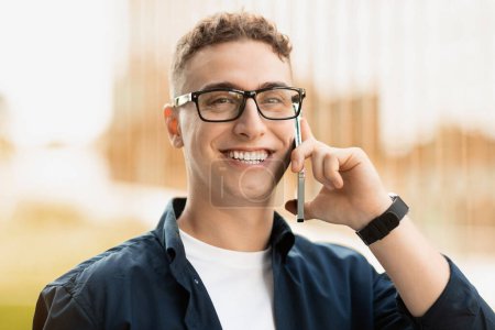 Photo for Smiling handsome millennial caucasian man in glass, enjoy lifestyle, calling by phone in city, outdoor. Good news, success business, work, study and conversation, close up - Royalty Free Image