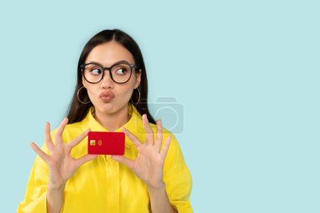 Photo for Shopping. Shopaholic Funny Young Lady Holding Credit Card Thinking What To Buy Posing Looking Aside At Free Space For Advertisement Text On Blue Studio Background. Sales And Discounts Offer - Royalty Free Image