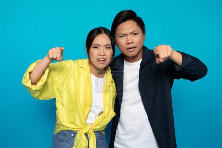 Téléchargez les photos : Confus triste couple asiatique sérieux dans les doigts de pointe occasionnels à la caméra, isolé sur fond de studio bleu. geste d'émotions, qu'est-ce que c'est, expression et question, espace libre - en image libre de droit