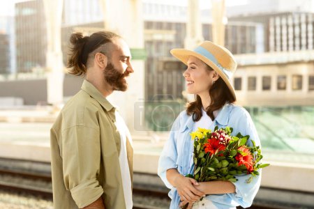 Photo for Positive young caucasian husband meets surprised lady, gives bouquet of flowers on train station. Love, relationship, travel lifestyle, dating romance, vacation and come back - Royalty Free Image